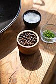 From above of bowl full of spices placed on wooden table near salt in kitchen with bright sunlight at home