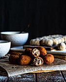 Delicious fried croquettes rolled in bread crumbs placed on piece of newspaper on wooden board
