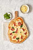 From above of tasty homemade pizza with basil and ham served on wooden cutting board on table