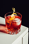 Glas mit bitterem alkoholischem Negroni-Cocktail, serviert mit Eis und Orangenschale auf weißer Fläche