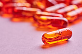 Composition of orange pills scattered on pink background in light studio