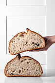 Crop anonymous person touching split sourdough bread with crunchy crust placed on white background
