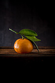 Whole unpeeled mandarin with pedicel and wavy foliage with pointed edges on wooden surface