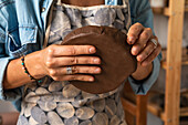 From above of crop anonymous male artisan molding clay piece while creating plate in workshop