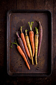 From above of baking tray with various whole unpeeled carrots with stalks on brown background