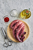 Top view of fresh raw octopus placed on round wooden plate near metal scissors spices and oil