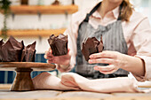 Crop unrecognizable female in apron showing baked dessert in paper liners in house kitchen