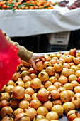Unbekannte Kundin wählt einen reifen roten Granatapfel aus, der an einem Sommertag auf einem Markt in der Stadt an einem Stand angeboten wird