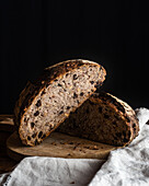 Freshly baked sliced sourdough bread loaf with walnuts and raising placed on white linen on black background