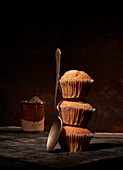 Tasty sweet baked muffins stacked on top of each other near spoon on black background