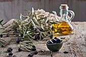 Schwarze Oliven und Krug mit Öl neben frischen Zweigen auf Holztisch in rustikaler Küche
