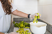Side view of cropped unrecognizable adult female cutting green fresh celery on cutting board using knife while cooking in kitchen at home