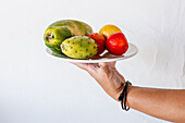 Crop unrecognizable person demonstrating plate with appetizing ripe papaya prickly pear and nectarines against white background