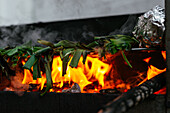 Haufen traditioneller katalanischer frischer grüner Kalzotten auf schwarzem Metallgrill mit Folie und glühender Holzkohle auf der Terrasse