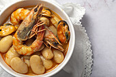 From above bowl with typical stew of beans with prawns, shrimps and mussels on a lace tablecloth and on a stone table