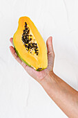 Crop unrecognizable person demonstrating whole fresh ripe papaya on sunny day against white background