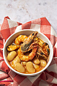 From above bowl with typical stew of beans with prawns, shrimps and mussels on a red checkered on a stone table