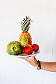 Crop unrecognizable person demonstrating plate with appetizing ripe pineapple papaya prickly pear and nectarines against white background
