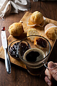 Cropped unrecognizable person holding mug with coffee and eating delicious homemade muffins with raspberry jam on wooden board on table