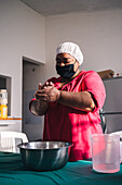 Venezuelan female in cloth face mask preparing arepas at table with bowl at home