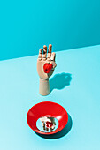 From above artificial hand with hot habanero pepper placed near red bowl with round mirror on blue background