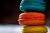 Close up of colorful French macaroons with various fillings placed on wooden table in dark background