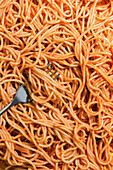 From above appetizing spaghetti with red sauce and fork on yellow background