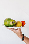 Crop unrecognizable person demonstrating plate with appetizing ripe papaya prickly pear and nectarines against white background