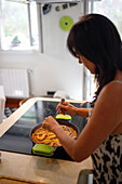 High angle of mature female checking delicious paella on stove while cooking lunch in sunlit kitchen at home
