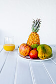 Delicious halved papaya served on plate near assorted colorful fruits and glass of fresh orange juice placed in white table