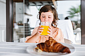 Vorschulisches braunhaariges Mädchen trinkt leckeren Orangensaft aus einem Glas in einer Cafeteria