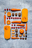Stilleben mit verschiedenen, aufeinander abgestimmten Herbstgemüsen, geschnittenen Kürbissen, Tomaten, Karotten, Mandarinen, Himbeeren und Haselnüssen von oben