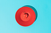 Top view of red bowl with hot habanero pepper placed on blue background