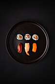 Blick von oben auf leckere Rollen und Nigiri-Sushi auf einem runden Teller auf schwarzem Hintergrund serviert