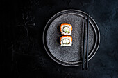 From above black stone plate with asian rolls and chopsticks