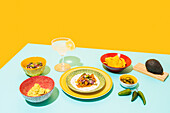 Dishware with nachos and chicken salad placed near bottle of beer and glass of lemonade against yellow background
