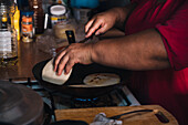 Side view of crop unrecognizable ethnic female preparing Venezuelan arepas in pan on gas stove in kitchen