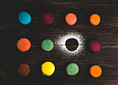 From above colorful French macaroons with various fillings placed on wooden table near powder sugar in dark background