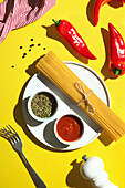 From above appetizing fresh dry spaghetti with red sauce and spice dip red peppers on yellow background