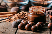 Verschiedene Schokoladenbonbons und ein Glas Mousse auf einem Holztisch mit einem Löffel mit Kakaopulver und Zimtstangen