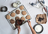 Draufsicht auf anonyme Hände, die mit Schokolade gebackene Kekse auf einem Metallgestell bestreichen