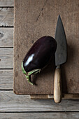 Fresh ripe eggplant with knife laid on wooden chopping board on box