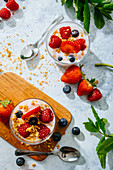 Blick von oben auf köstlichen hausgemachten Joghurt mit Erdbeeren, Beeren und Müsli auf weißem Hintergrund