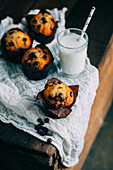 Delicious muffins with chocolate chips and a glass of milk on dark wooden background