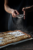 Crop shot of woman covering freshly baked frangipane apple pie with powdered sugar on wooden table