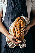 Crop unrecognizable male baker in apron demonstrating loaf of fresh crispy bread in kitchen