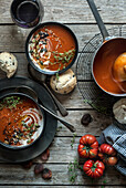 Flat lay of bowls with creamy tomato soup garnished with seeds and served on table with tomatoes and dried apricots