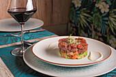 Roter Thunfischtartar mit Soße auf einem Teller und einem Glas Rotwein auf einem Tisch im Restaurant