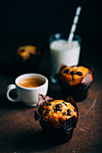 Chocolate muffins, milk and coffee cup on dark background