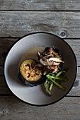 Top view of served round bowl with eggplant and shiitake mushrooms on wooden table with silver cutlery